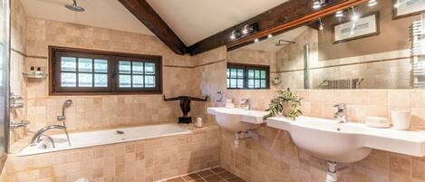 A modern bathroom with a bathtub, two sinks, a large mirror, and a window.