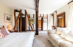 A bedroom with a bed, a sofa, wooden beams, a lamp, and a framed picture on the wall.