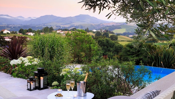 A patio with a table set for two, a champagne bottle, and a view of a mountainous landscape. - Villa Souraïde with pool, games room and Basque views (Souraide)