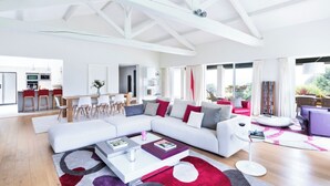 A spacious living area with a large white sectional sofa, a dining table with chairs, and a kitchen area. - Villa Souraïde with pool, games room and Basque views (Souraide)