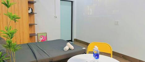 A room with a bed, a small table with a remote control, a water bottle, and a potted plant.