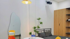 A compact room with a bed, a small table with chairs, an air conditioning unit, and a plant. - Corgi House Da Nang- Airport City Center (Da Nang)