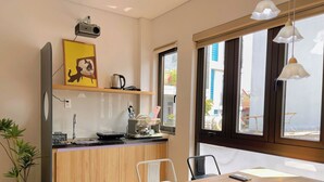 A modern kitchen with a wooden countertop, a coffee machine, and a small island with a sink. There is a dining area with a wooden table and chairs, and a large window providing a view of the outside. - Corgi House Da Nang- Airport City Center (Da Nang)