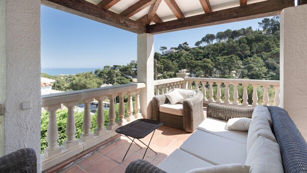 A balcony with a wicker sofa, a small table, and a view of a hillside. - Villa with Pool 700 Meters from the Beach (Begur)