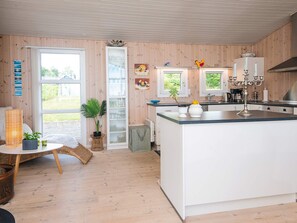 Eine moderne Küche mit Holzwänden, einer zentralen Kochinsel und einem Essbereich mit einem Korbstuhl-Tisch und -stühlen.