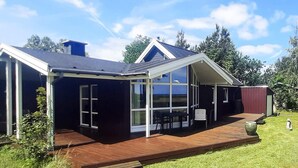 Een modern huis met een groot raam, een houten terras en een donkere gevel.