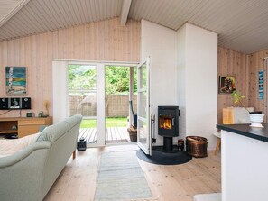 Ein gemütliches Wohnzimmer mit einer Couch, einem Kamin, einem Essbereich und Blick ins Freie.