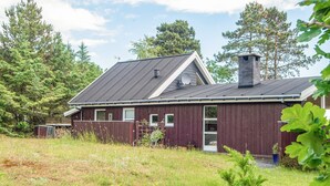 Een rood houten huis met een grijs dak, omringd door begroeiing en bomen.