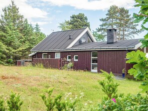 A red wooden house with a grey roof, surrounded by greenery and trees. - 5 Star Holiday Home in Hadsund (Hadsund)