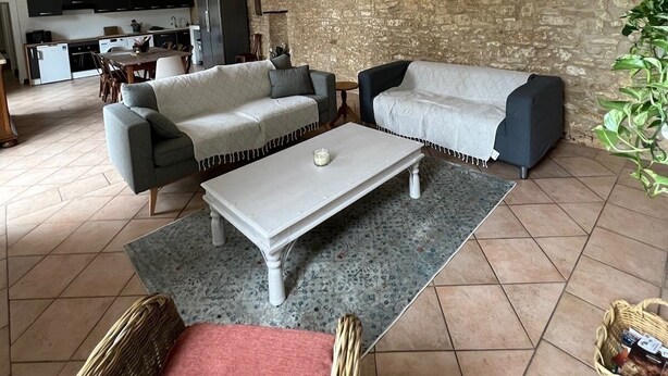 A living room with a stone wall, a dining area, and a kitchen in the background. - Large family home (Savignac-les-Églises)