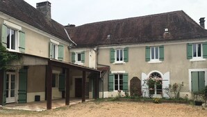 A two-story building with a covered patio area, a gravel courtyard, and a garden with flowers. - Large family home (Savignac-les-Églises)