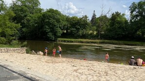 A sandy beach area with a body of water, trees, and a stone wall. - Large family home (Savignac-les-Églises)