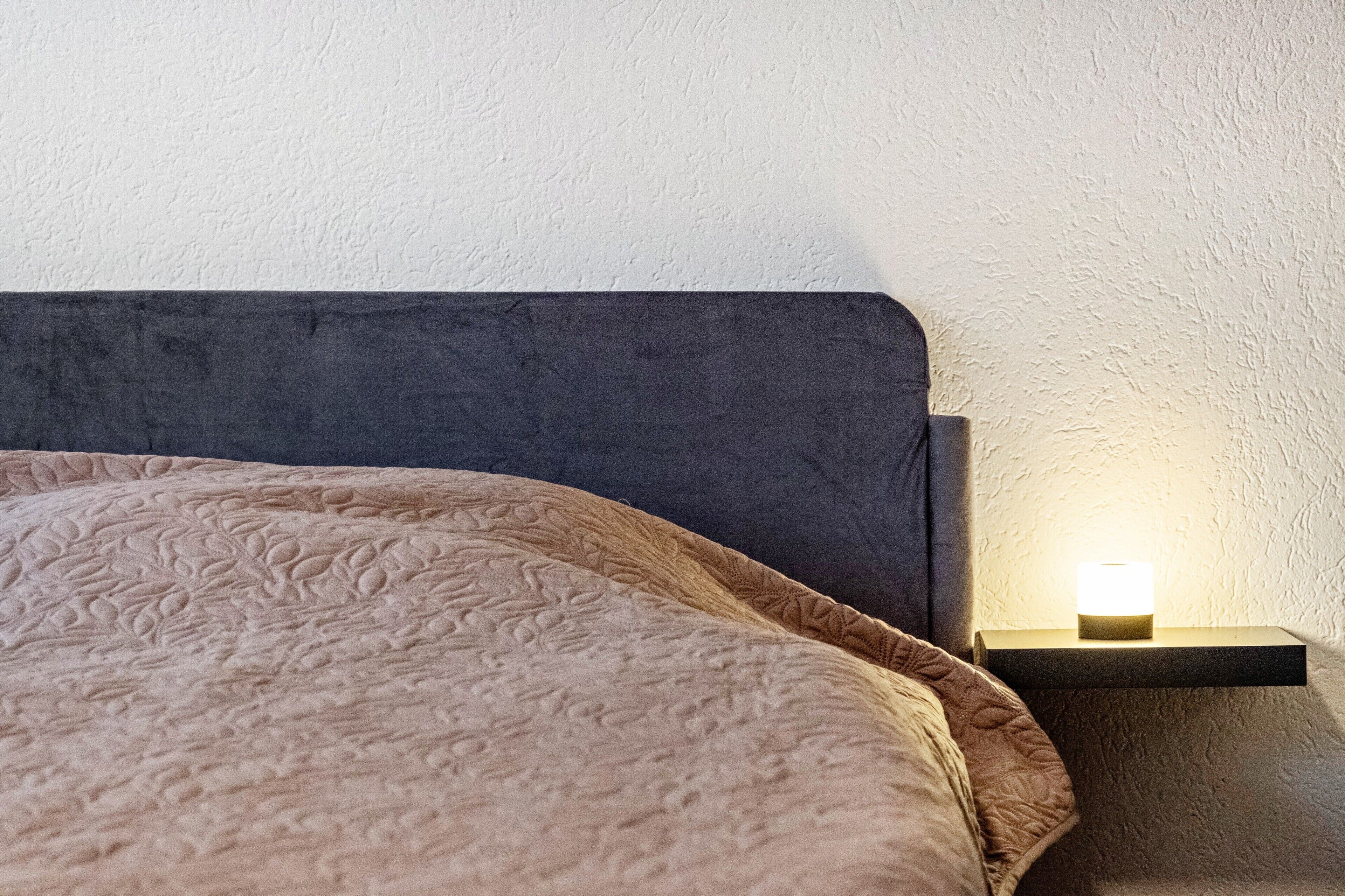 A bed with a textured blanket, a dark headboard, and a bedside table with a lamp.