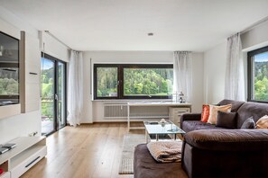 Ein modernes Wohnzimmer mit einem großen Fenster, einem Sofa, einem Glastisch und einem weißen Schreibtisch.