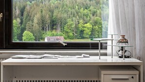 A desk with papers, a lamp, and a view of a forest through a window.