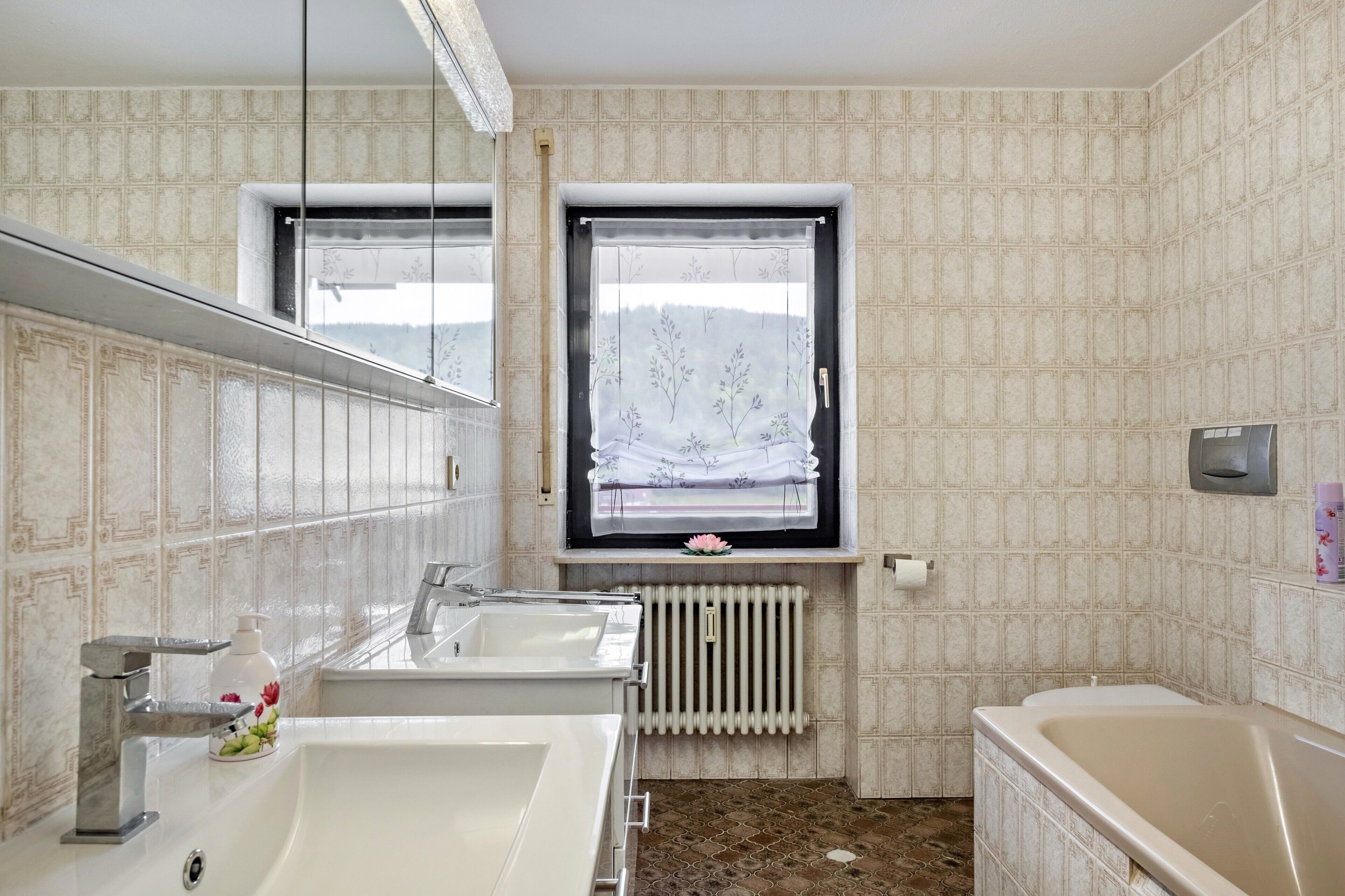 Ein Badezimmer mit zwei Waschbecken, einem Fenster mit Aussicht, einem Heizkörper und einer Badewanne.