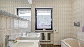Ein Badezimmer mit zwei Waschbecken, einem Fenster mit Aussicht, einem Heizkörper und einer Badewanne.