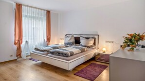 A modern bedroom with a bed, bedside table, lamp, and a vase of flowers.