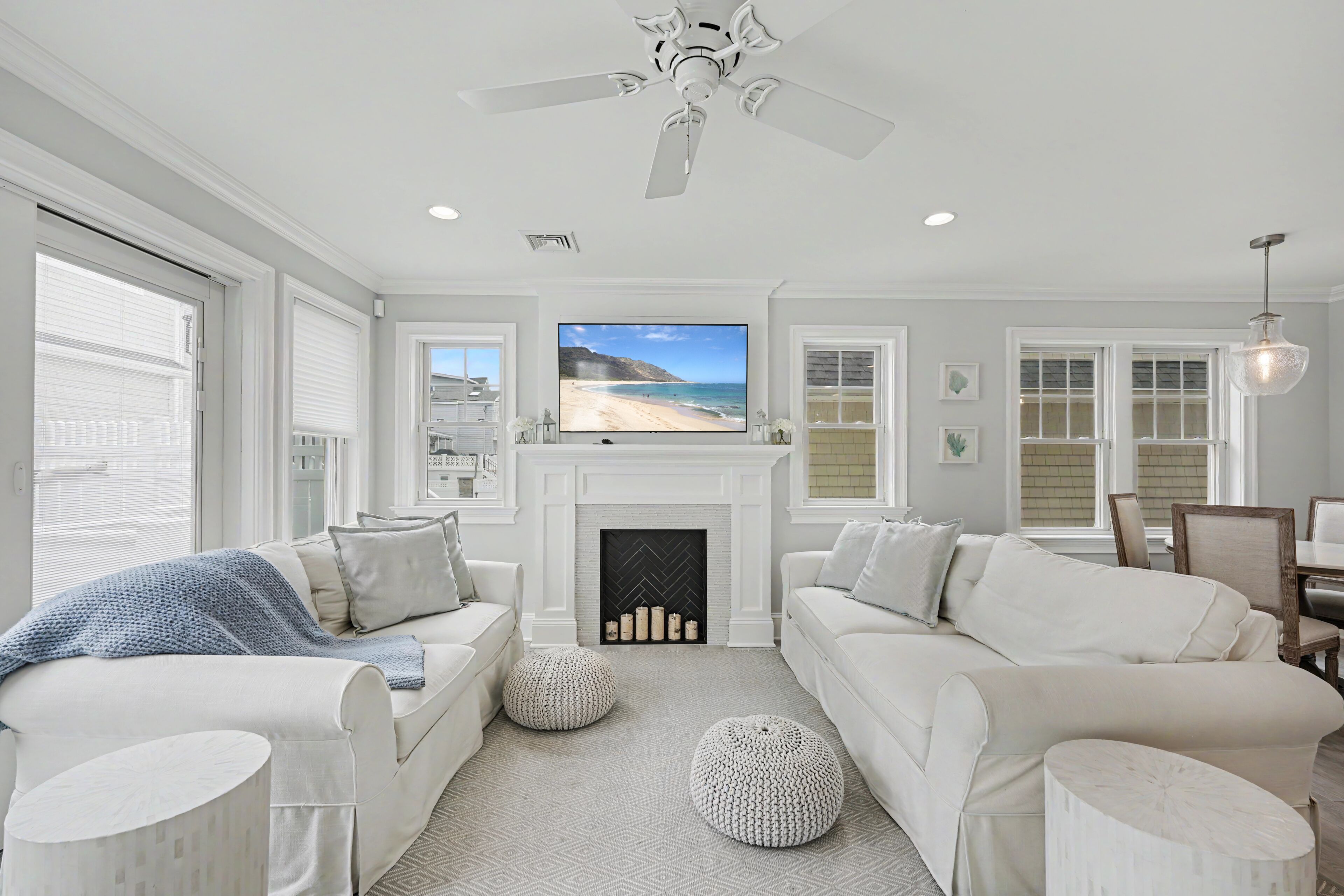 A living room with a fireplace, white sofas, a television, and a ceiling fan.