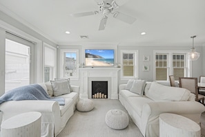 A living room with a fireplace, white sofas, a television, and a ceiling fan. - Stunning Manasquan getaway featuring a private pool and hot tub where comfort meets coastal luxury. (Manasquan)