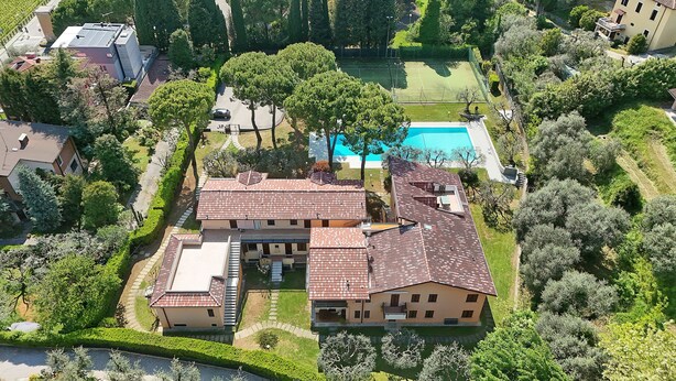 Una casa grande con piscina, rodeada de árboles y una cancha de tenis.
