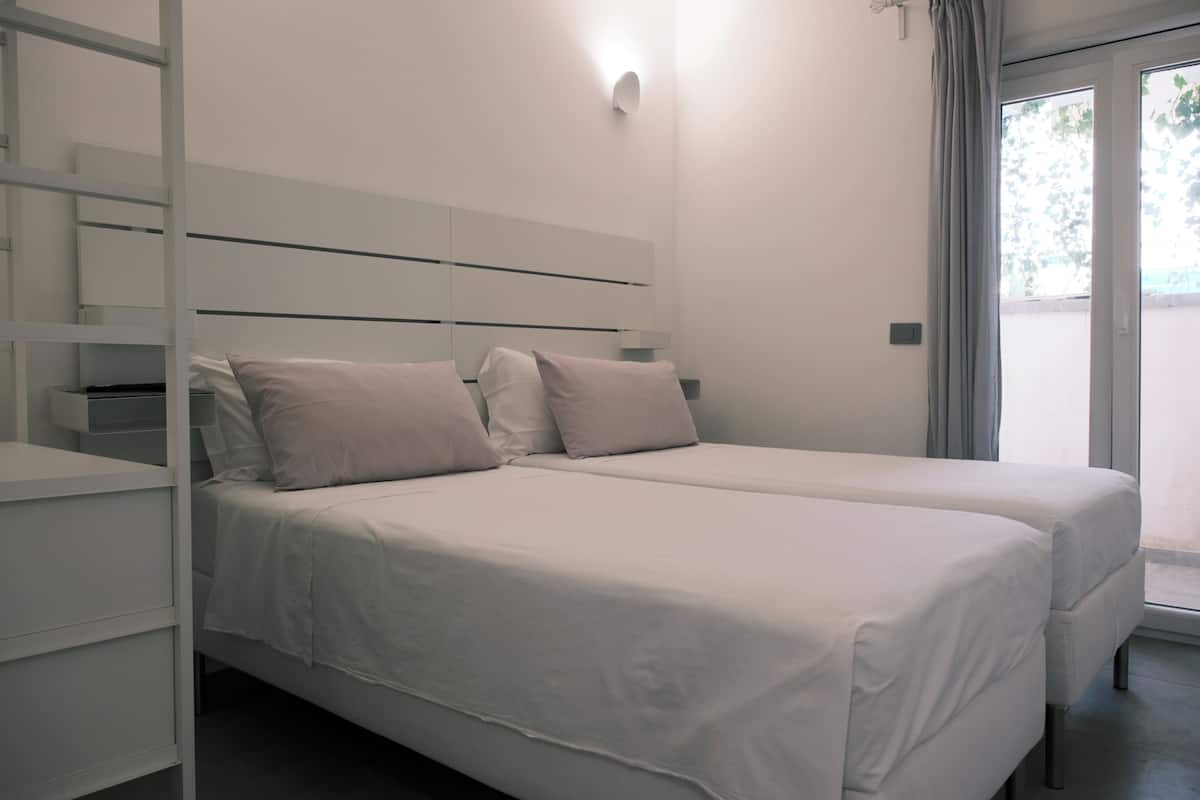 Ein Schlafzimmer mit zwei Betten, einem Nachttisch, einer Wandleuchte und einem Fenster mit Vorhängen.