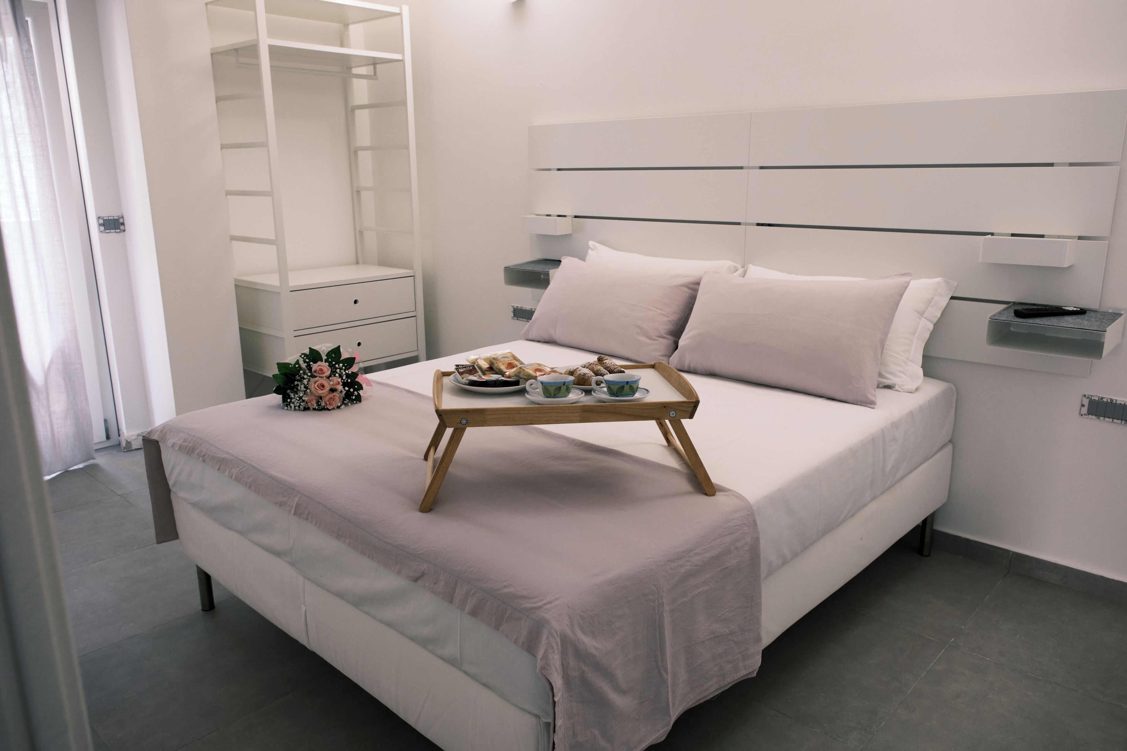 Un dormitorio moderno con cama, mesitas de noche, un armario y una bandeja con objetos sobre la cama.