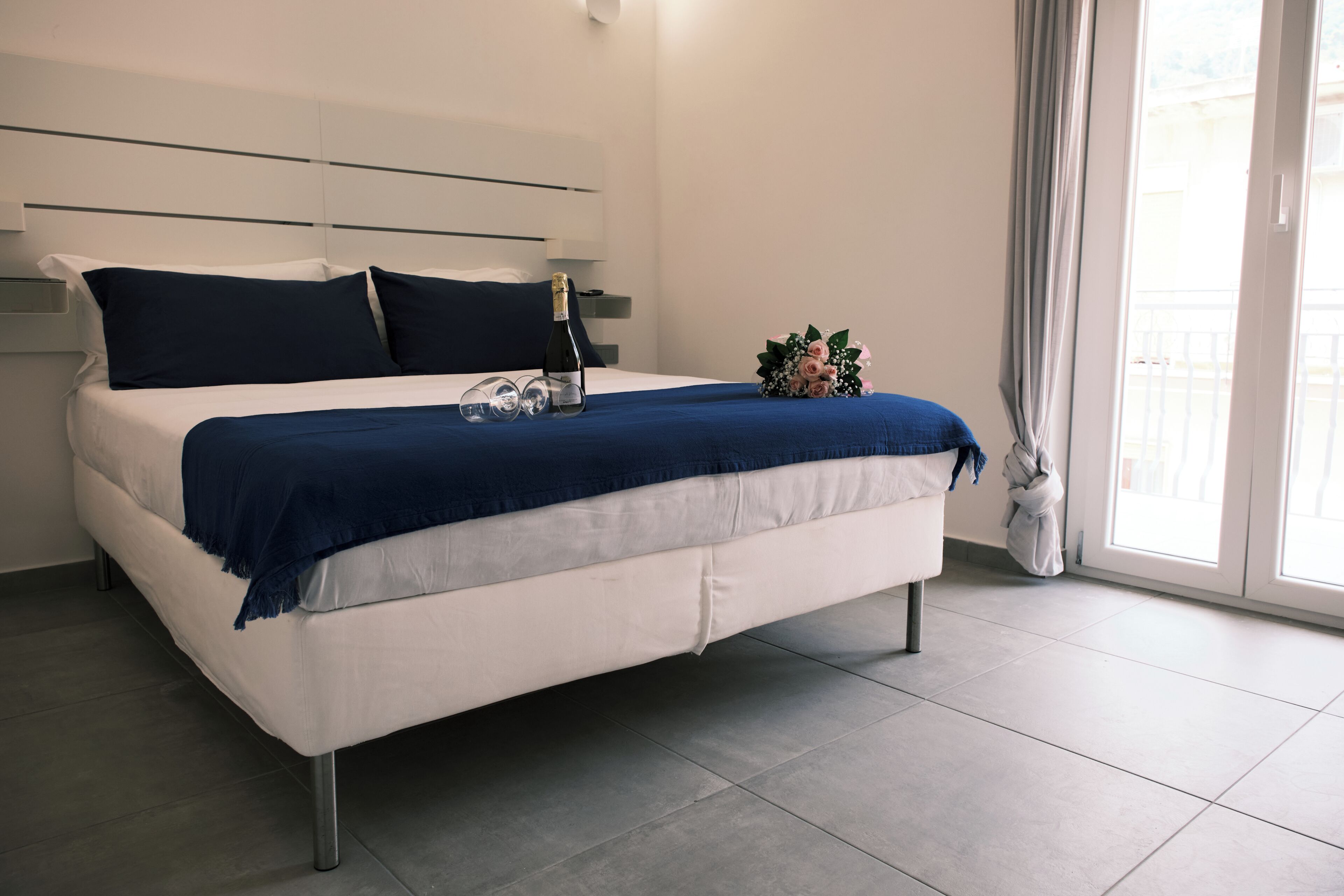 A modern bed with a blue blanket, a bottle, and a bouquet of flowers.