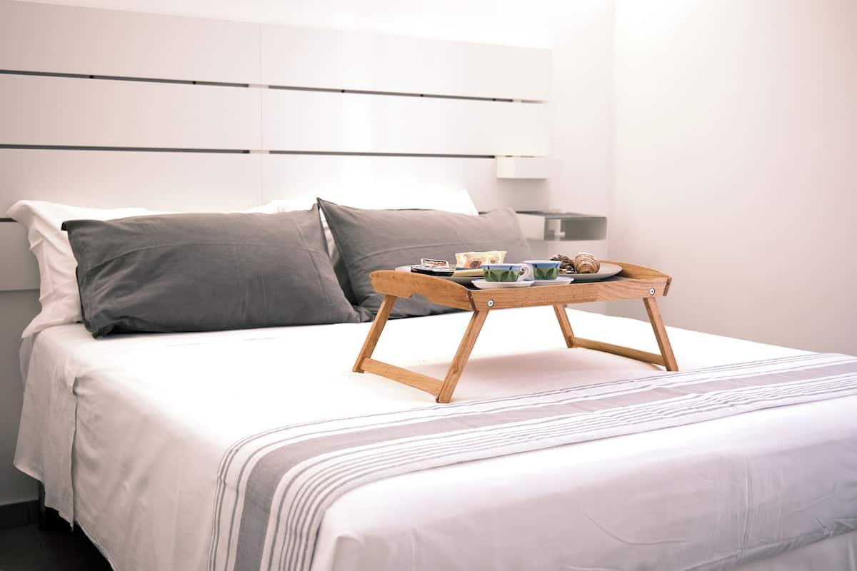 Ein ordentlich bezogenes Bett mit einem Holztablett, das eine Platte, eine Tasse und eine kleine Schüssel trägt.