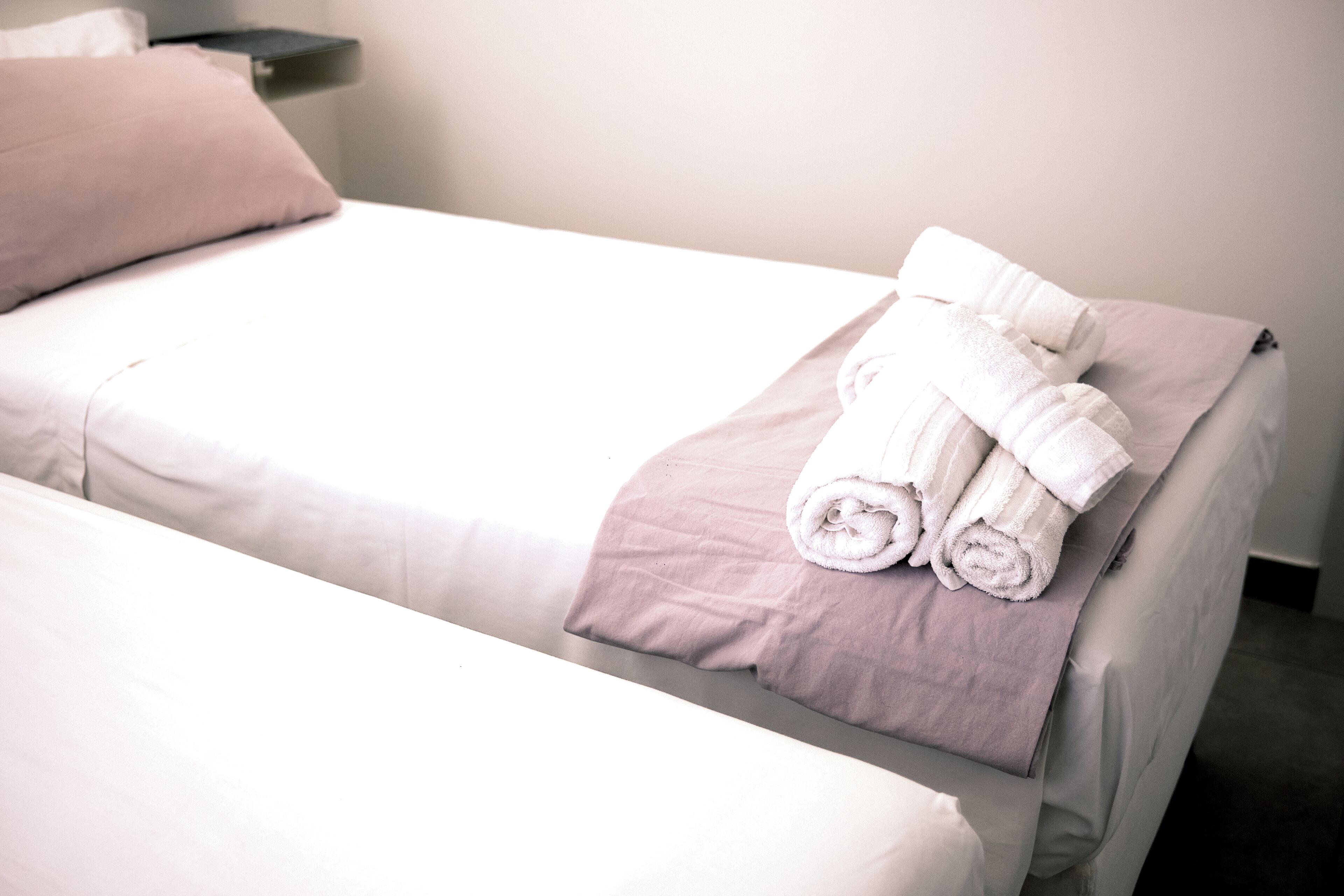Camera d'albergo con due letti, ognuno con un cuscino e un asciugamano arrotolato.