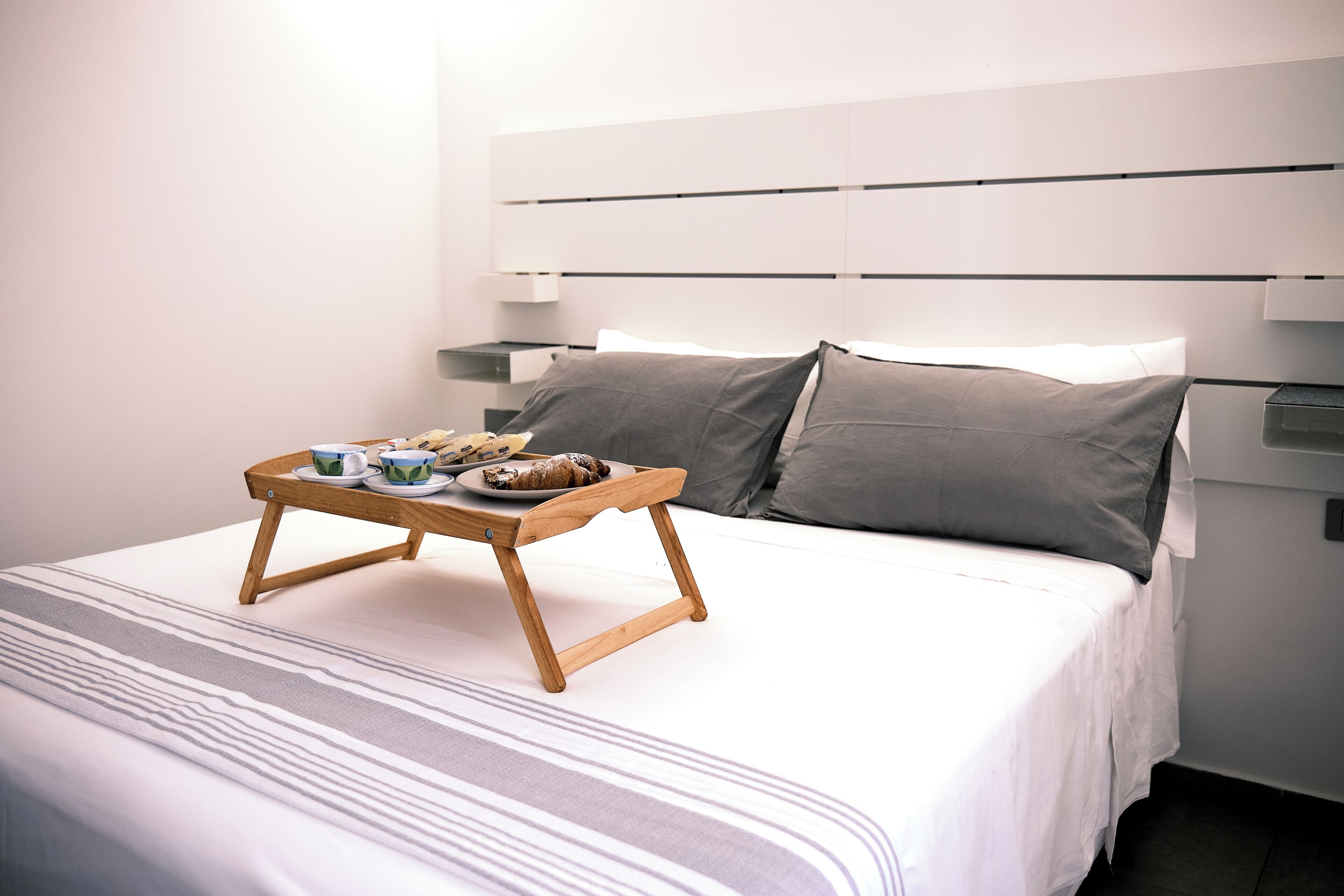 A neatly made bed with a tray of breakfast items, a bedside table, and a modern headboard.