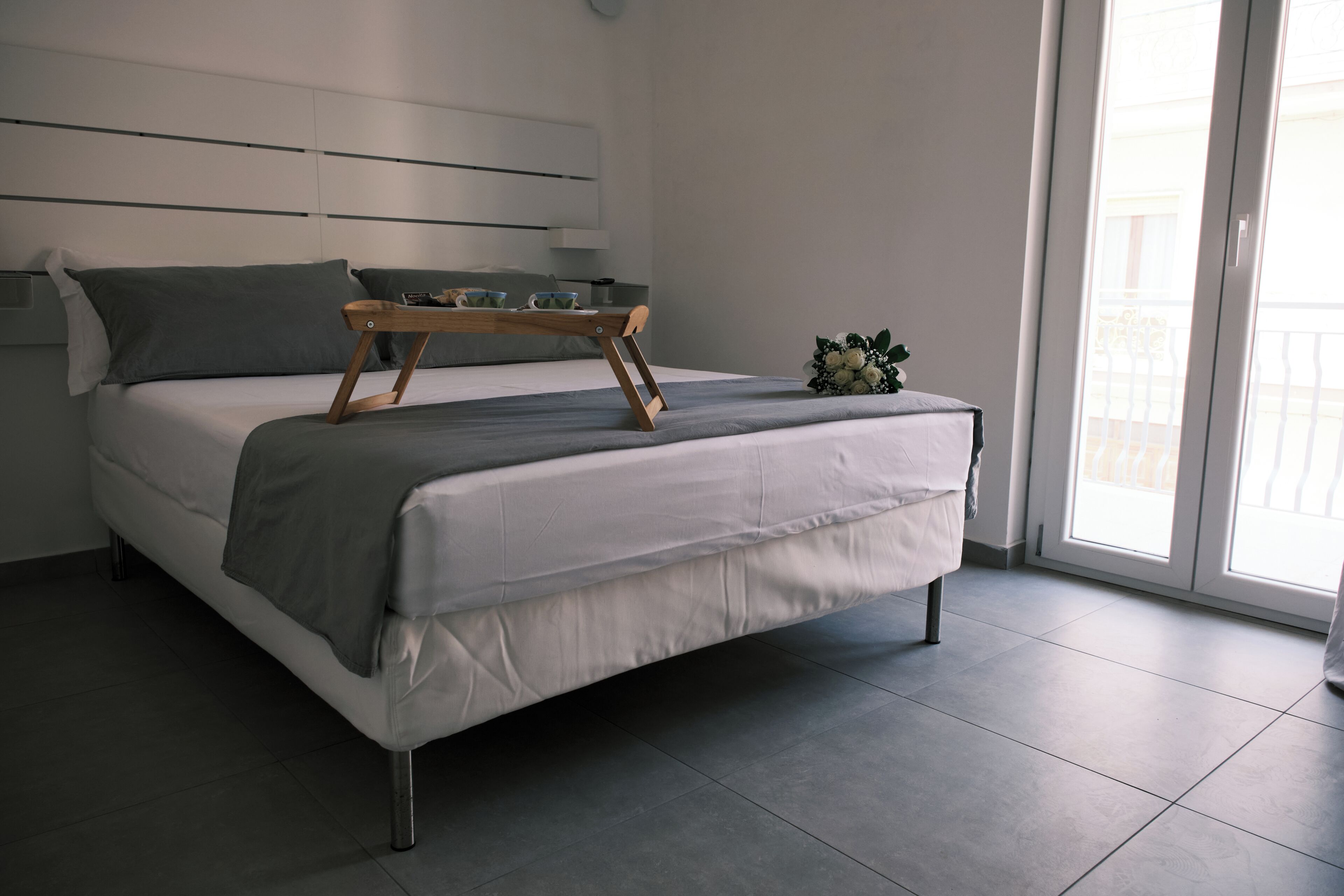 A modern bedroom with a bed, a wooden tray, and a bouquet of flowers.