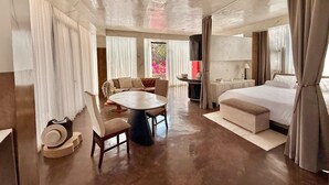 A spacious room with a large bed, a dining table, and a seating area.