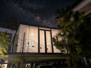 A building with a balcony, a starry night sky, and palm trees.