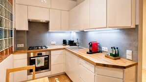 A modern kitchen with white cabinets, a gas stove, an oven, a coffee maker, and a sink. - City View Apartment near Nowy Świat (Warsaw)