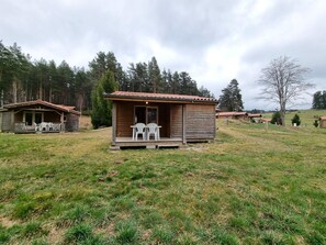 A small wooden cabin with a porch and two white chairs, surrounded by a grassy field and trees. - Chalet pets allowed - 4 guests (Usson-en-Forez)