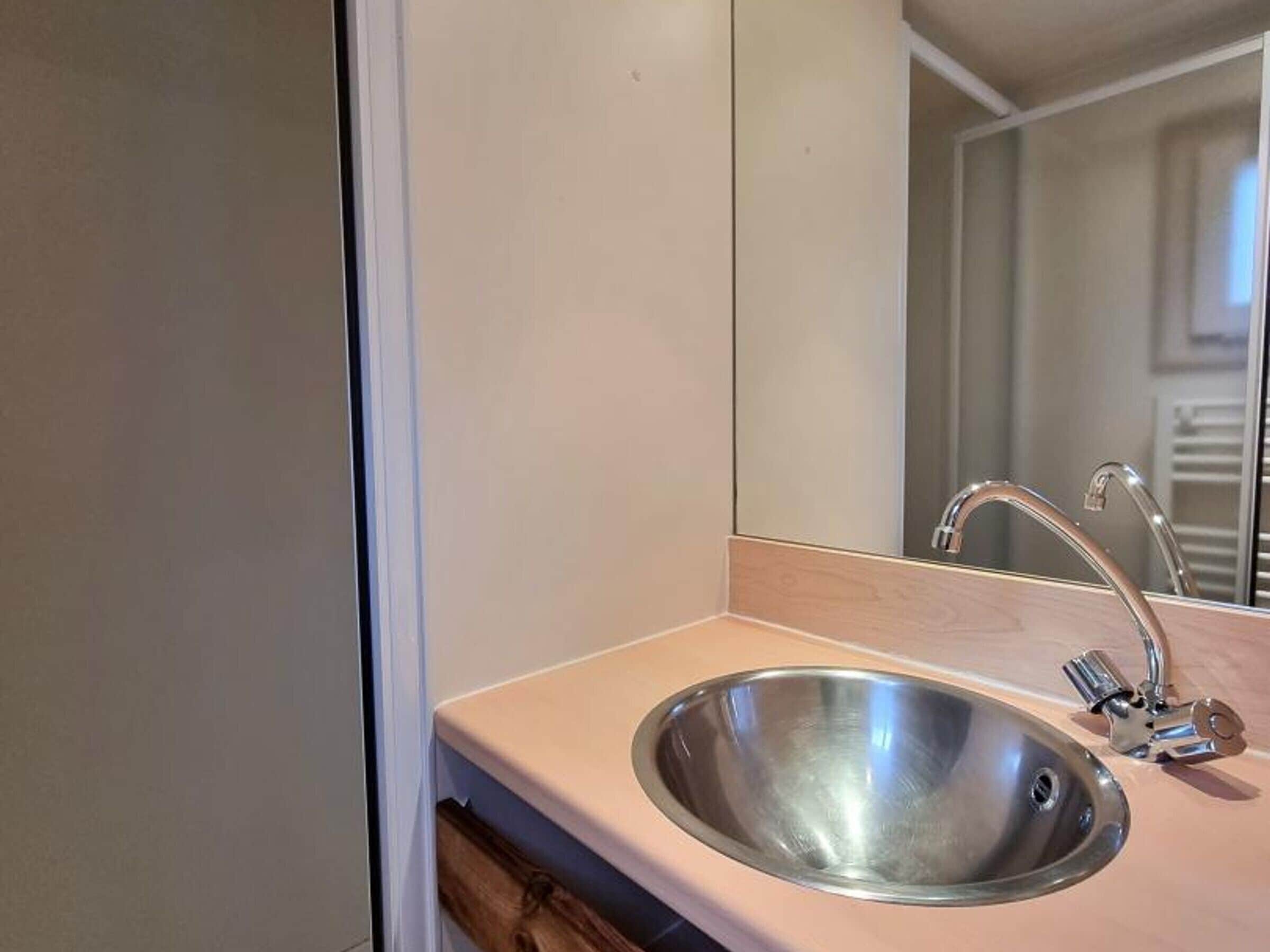 Une salle de bain avec un lavabo en acier inoxydable, un miroir et un meuble en bois.