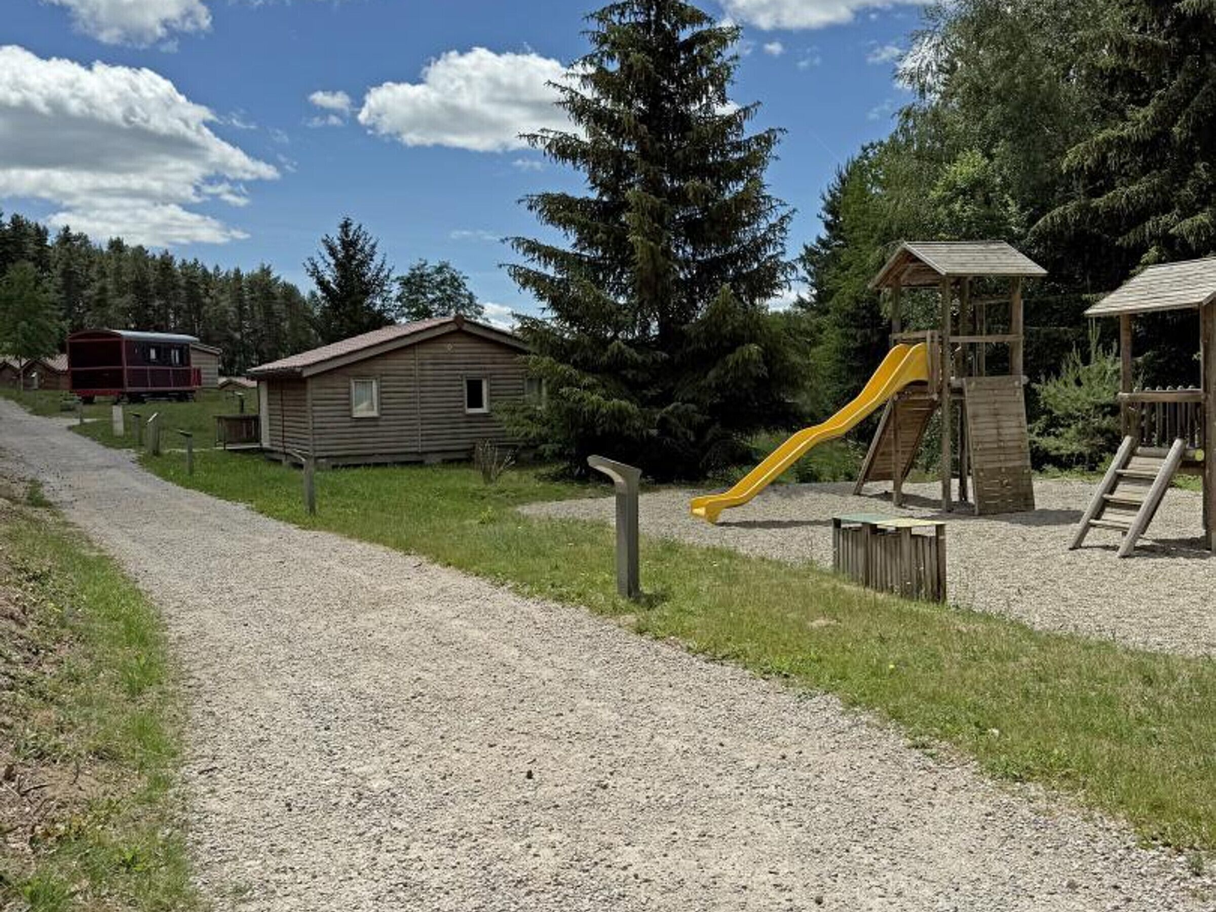 Un camino de grava que lleva a una cabaña de madera y un parque infantil con un tobogán amarillo.