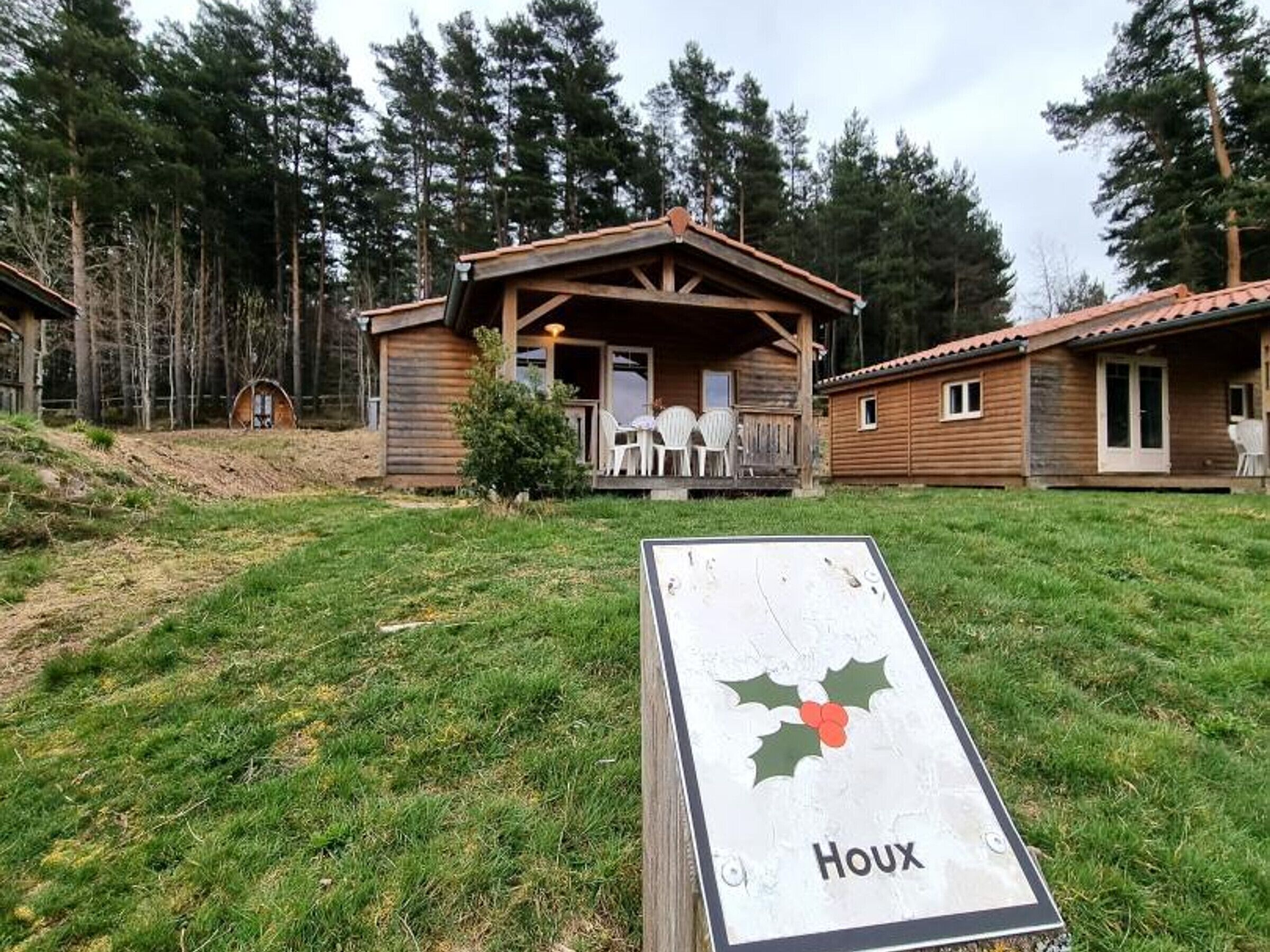 Een houten hut met een veranda en twee witte stoelen, gelegen in een grasveld met bomen.