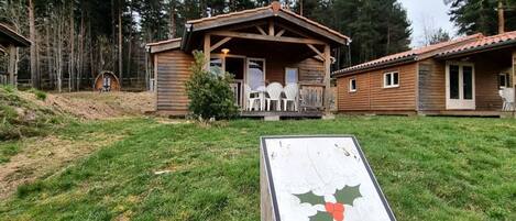 Een houten hut met een veranda en twee witte stoelen, gelegen in een grasveld met bomen.