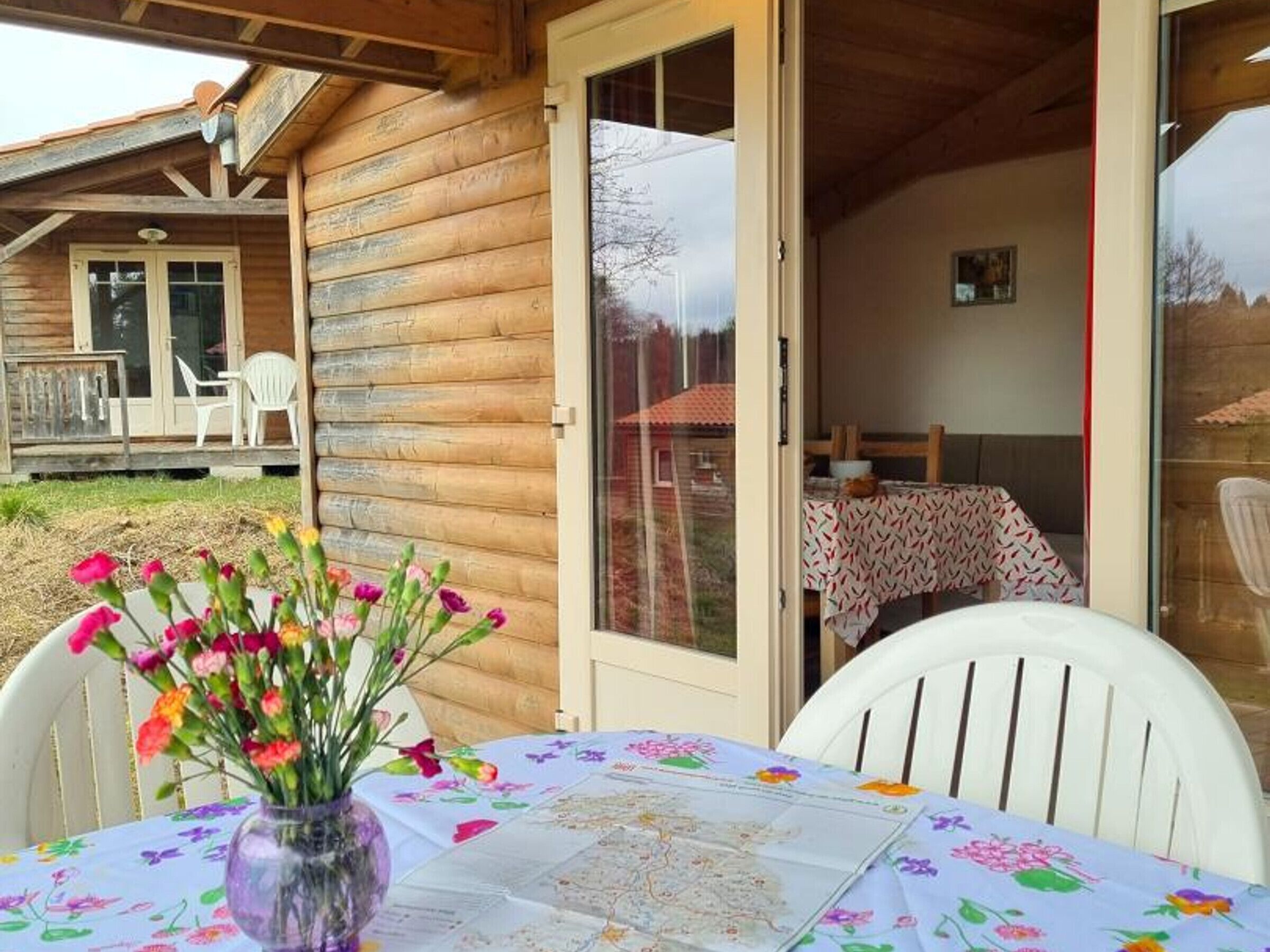 A wooden cabin with a dining area featuring a table with a floral tablecloth and a vase of flowers.