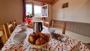 Un coin repas avec une table mise pour le petit-déjeuner, comprenant des croissants, une bouilloire et un saladier de fruits.