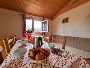 A dining area with a table set for breakfast, including croissants, a kettle, and a bowl of fruit. - Nature chalet, pets welcome - 6 guests (Usson-en-Forez)