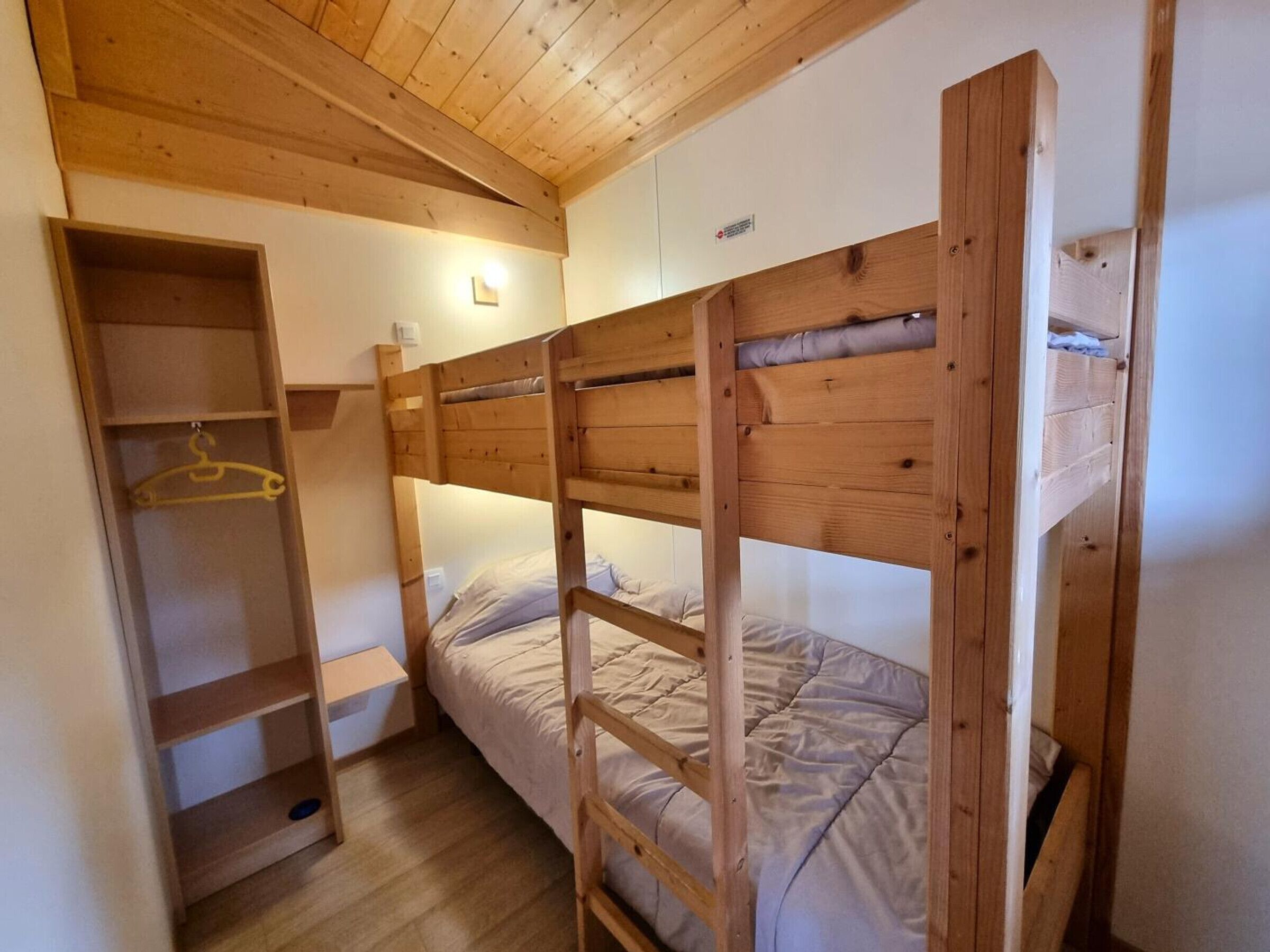 A bunk bed room with a wooden headboard, a shelf unit, and a small bedside table.
