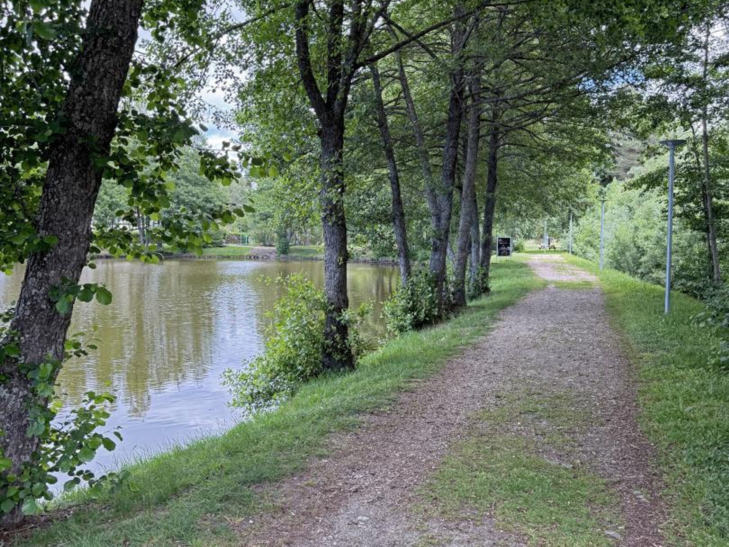 Un sentier de gravier longe un lac paisible, bordé d’arbres.