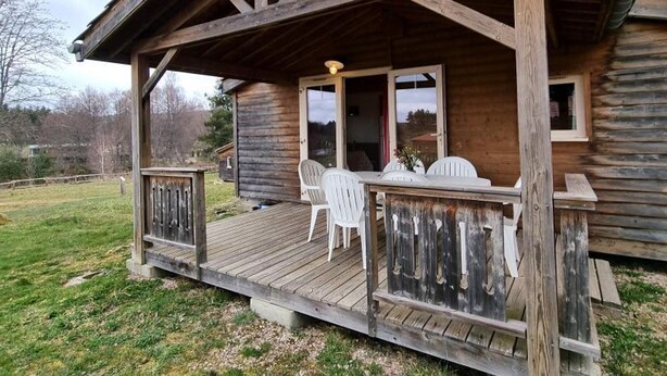 Une cabane en bois avec une véranda, une table à manger et deux chaises.