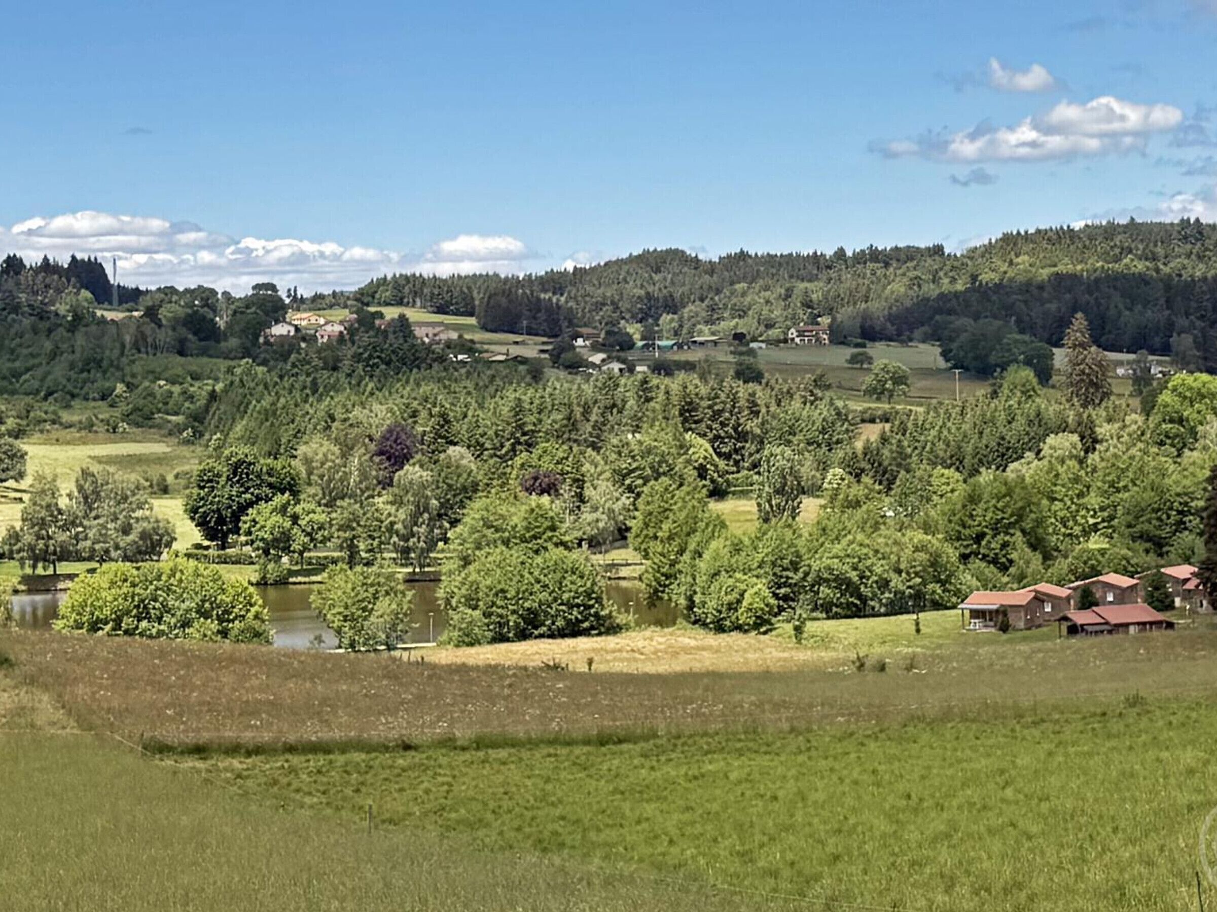 A rural landscape with a lake, trees, and a few buildings.