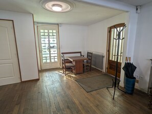 Une pièce avec un plancher en bois, une table à manger avec des chaises, une porte avec des panneaux de verre, un radiateur et un porte-manteau avec des parapluies.