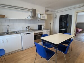 Une cuisine compacte équipée d’un lave-vaisselle, d’une cuisinière, d’un four à micro-ondes et d’un coin repas avec des chaises bleues.