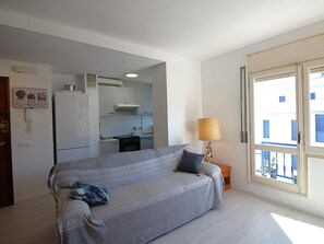 Habitación con sofá, lámpara, zona de cocina y ventana con vistas.